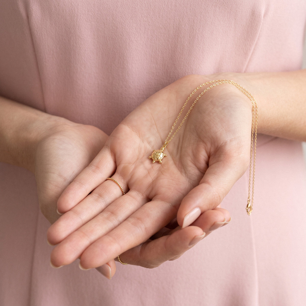 Sea turtle charm held in two cupped hands, chain spilling between the fingers