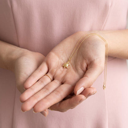Sea turtle charm held in two cupped hands, chain spilling between the fingers