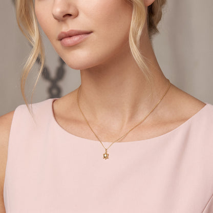 Turtle charm worn with a pink boat neck dress, the chain following the collarbone