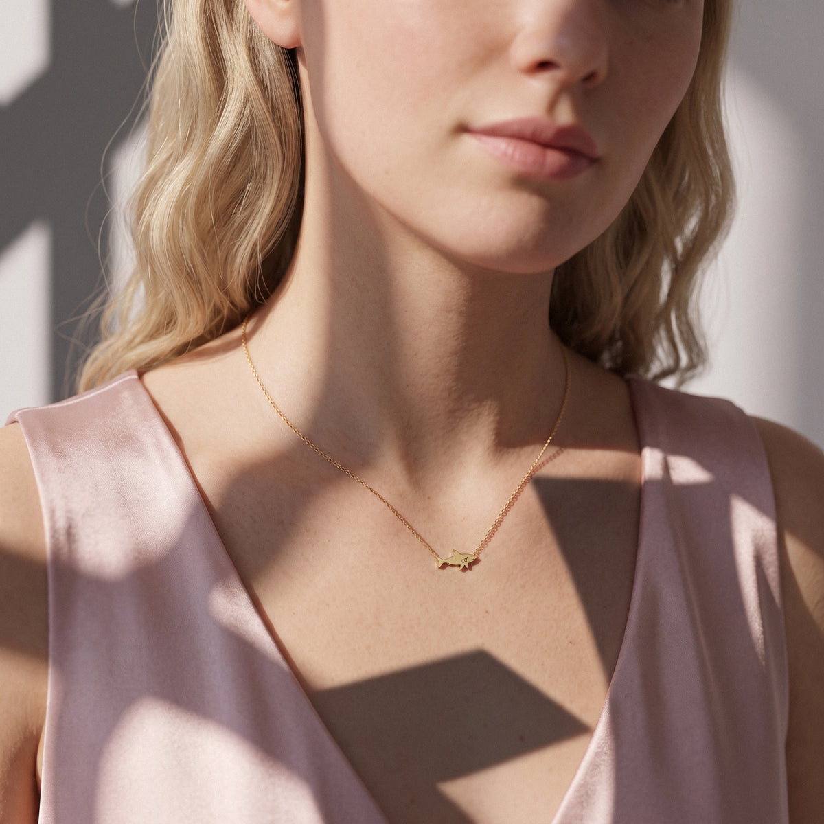 Minimal shark charm worn at the collarbone with a square-neck blush dress and window shadows