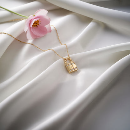 Diamond lock initial necklace laid on white silk beside a pink blossom, stones catching the light