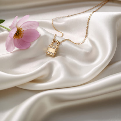 Gold padlock diamond necklace resting on ivory silk next to a lilac flower
