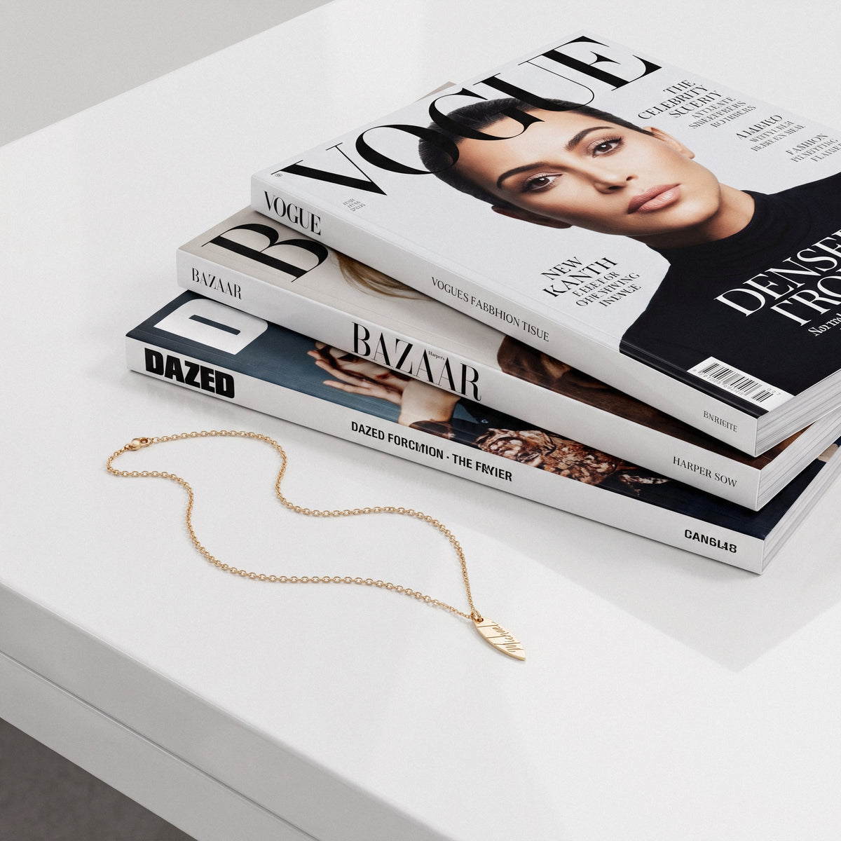Engraved surfboard chain draped over a pile of Vogue and Dazed issues