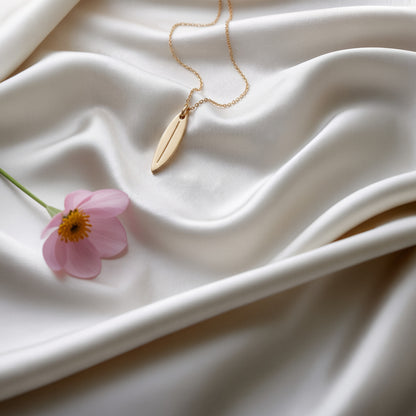 Surfboard necklace on ivory silk with a pink daisy, showing the board&