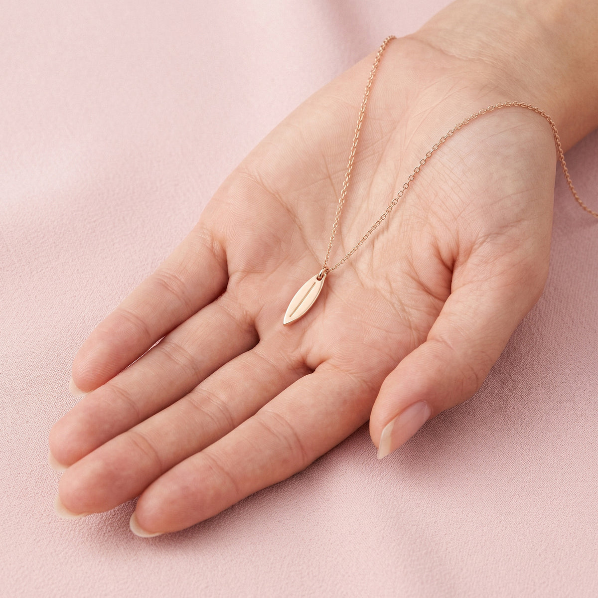 Slim gold surfboard pendant lying across an open palm