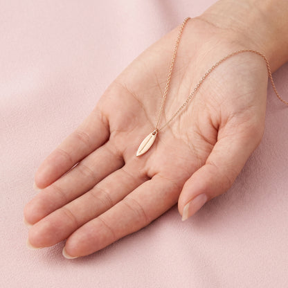 Slim gold surfboard pendant lying across an open palm