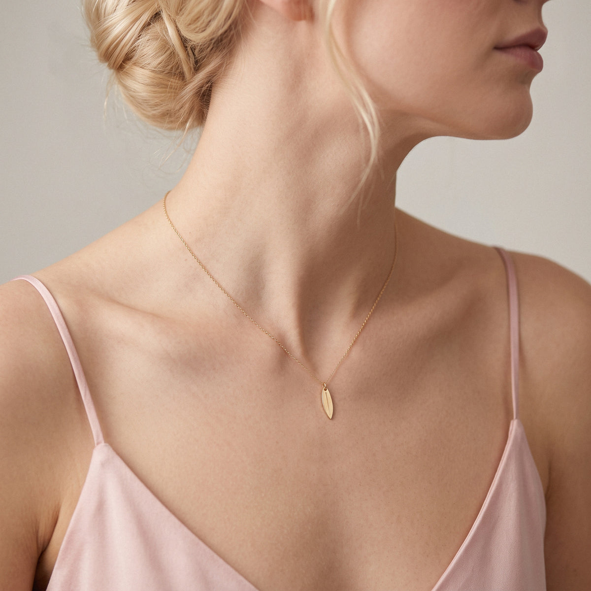 Hair pinned up and bare shoulders, with a slim gold surfboard charm catching the light below the neck
