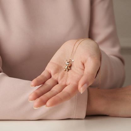 Voodoo doll charm held in an open palm against a dusty pink sleeve