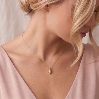 Voodoo doll necklace worn with a deep pink v-neck, charm resting below the collarbone