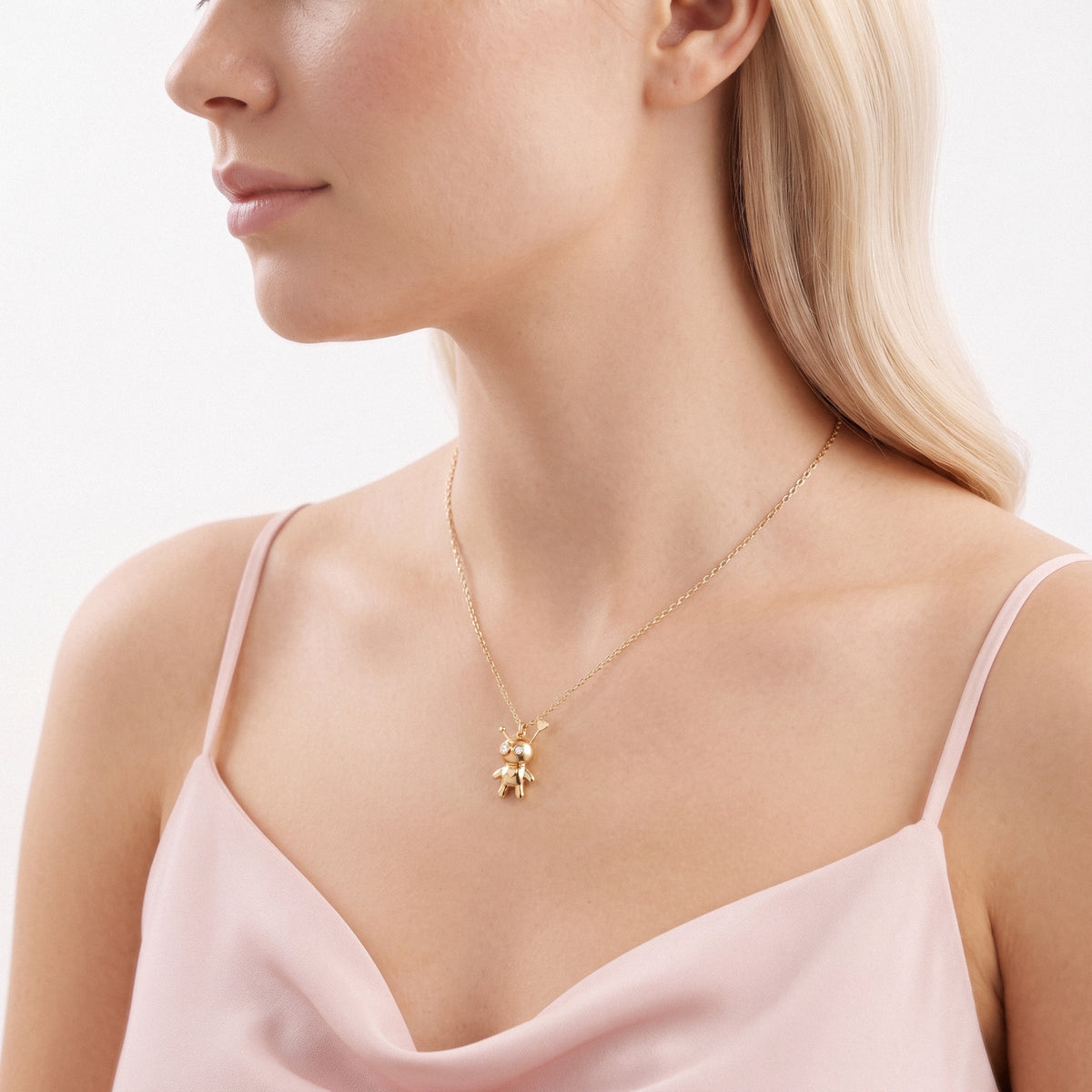 Side profile of a model with the doll talisman sitting against a pale pink strap top