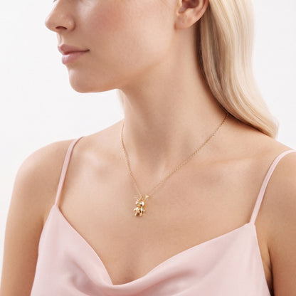 Side profile of a model with the doll talisman sitting against a pale pink strap top