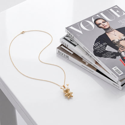 Doll pendant necklace laid out on Vogue and Bazaar magazines on a white table